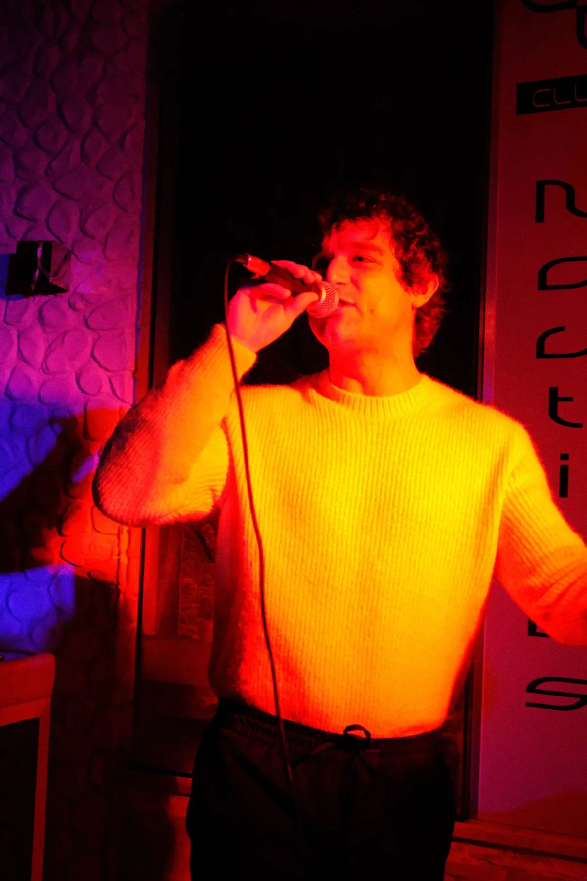 Cantante in giacca a righe al microfono, sotto una luce rossa e gialla
